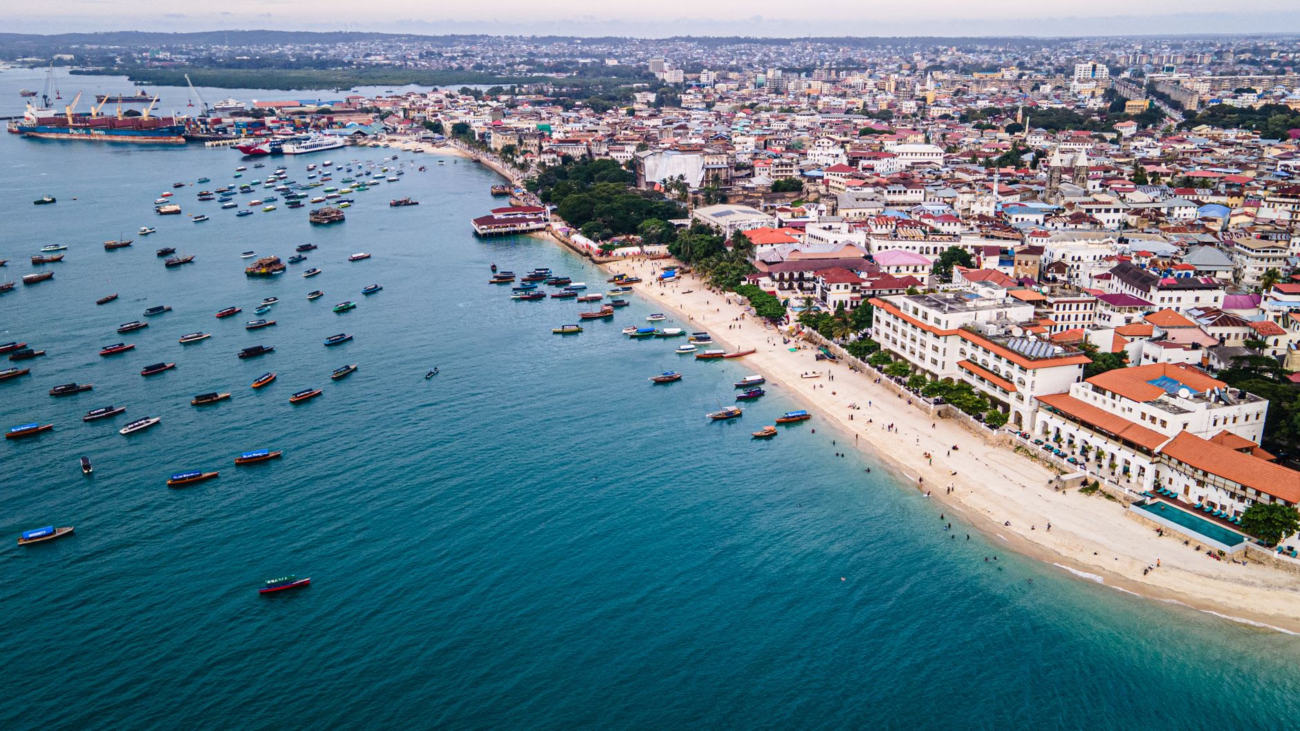 Vue aérienne du front de mer de Stone Town, ses toits de tôle et de tuiles et une centaine de barques mouillées le long de la plage