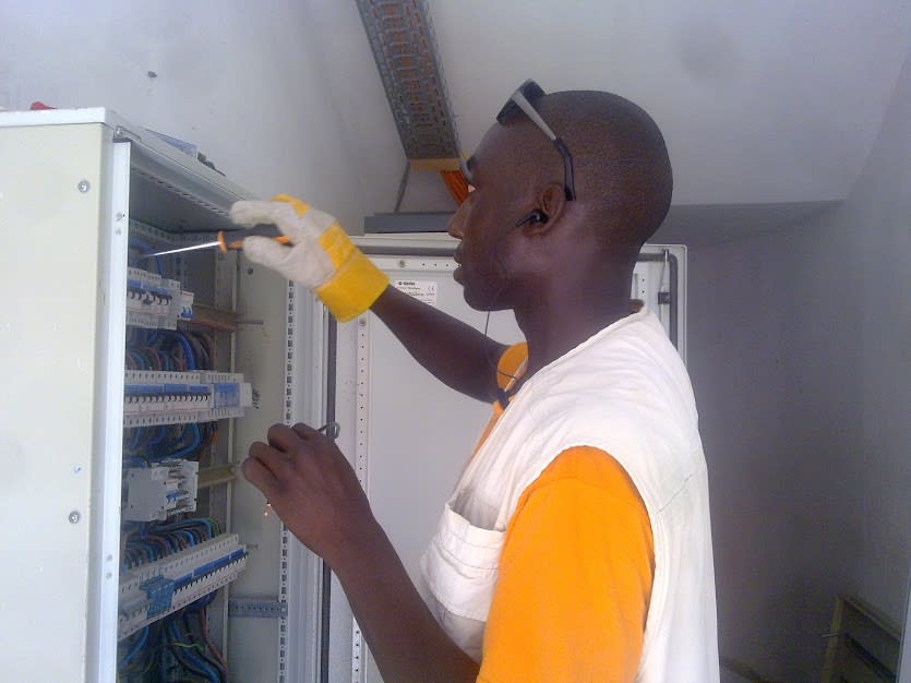 Technicien ENERCOS câblant une armoire de distribution électrique équipée de disjoncteurs modulaires.