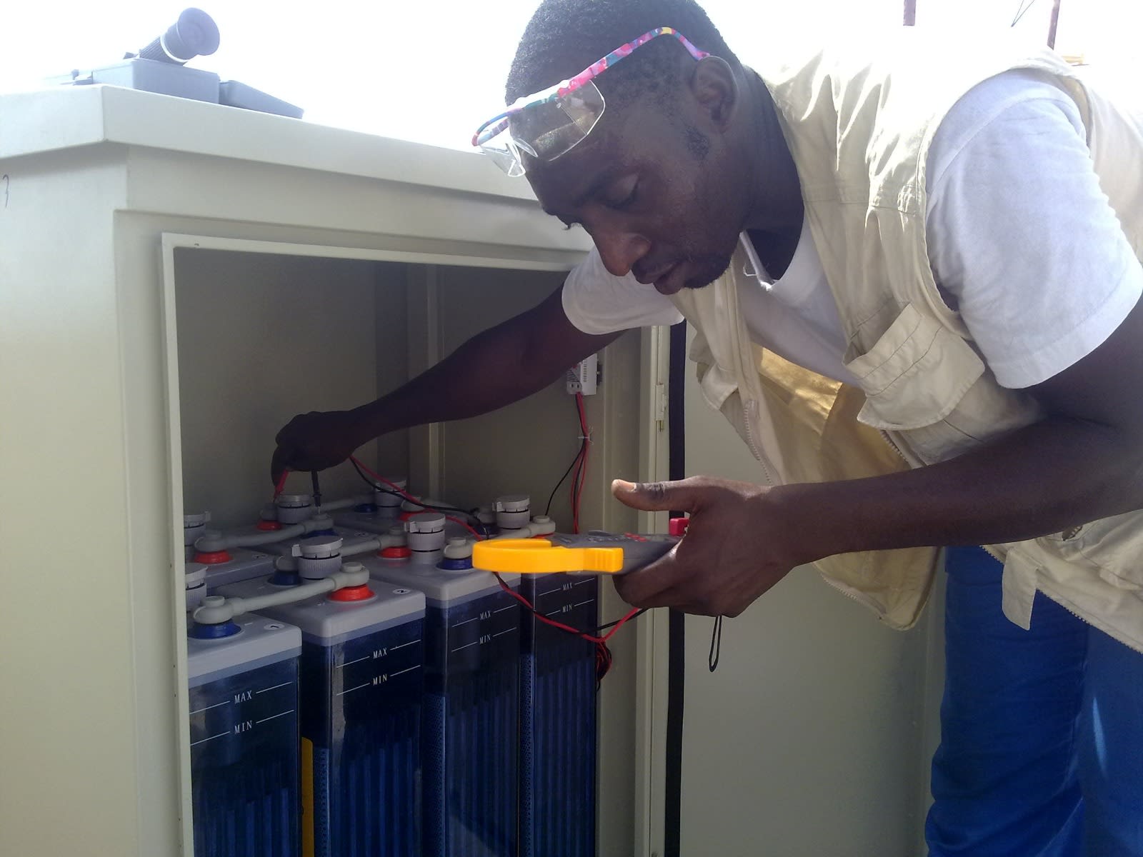 Technicien ENERCOS contrôlant un parc de batteries de stockage (OPzS) au multimètre à pince.