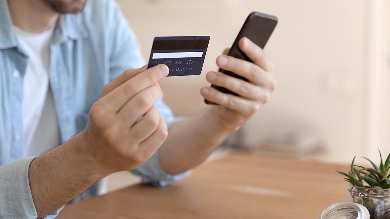 Man holding credit card in one hand and a smartphone in the other.