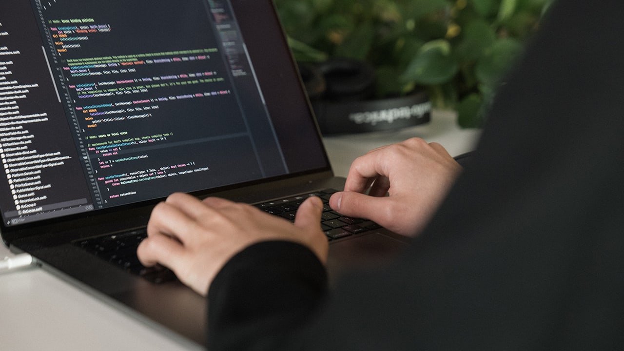 close up of hand and laptop with programming ide onscreen