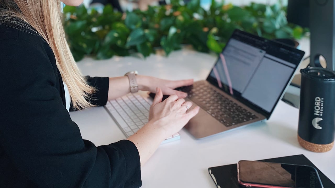 woman works on laptop with nord security bottle off to the side and greenery in background