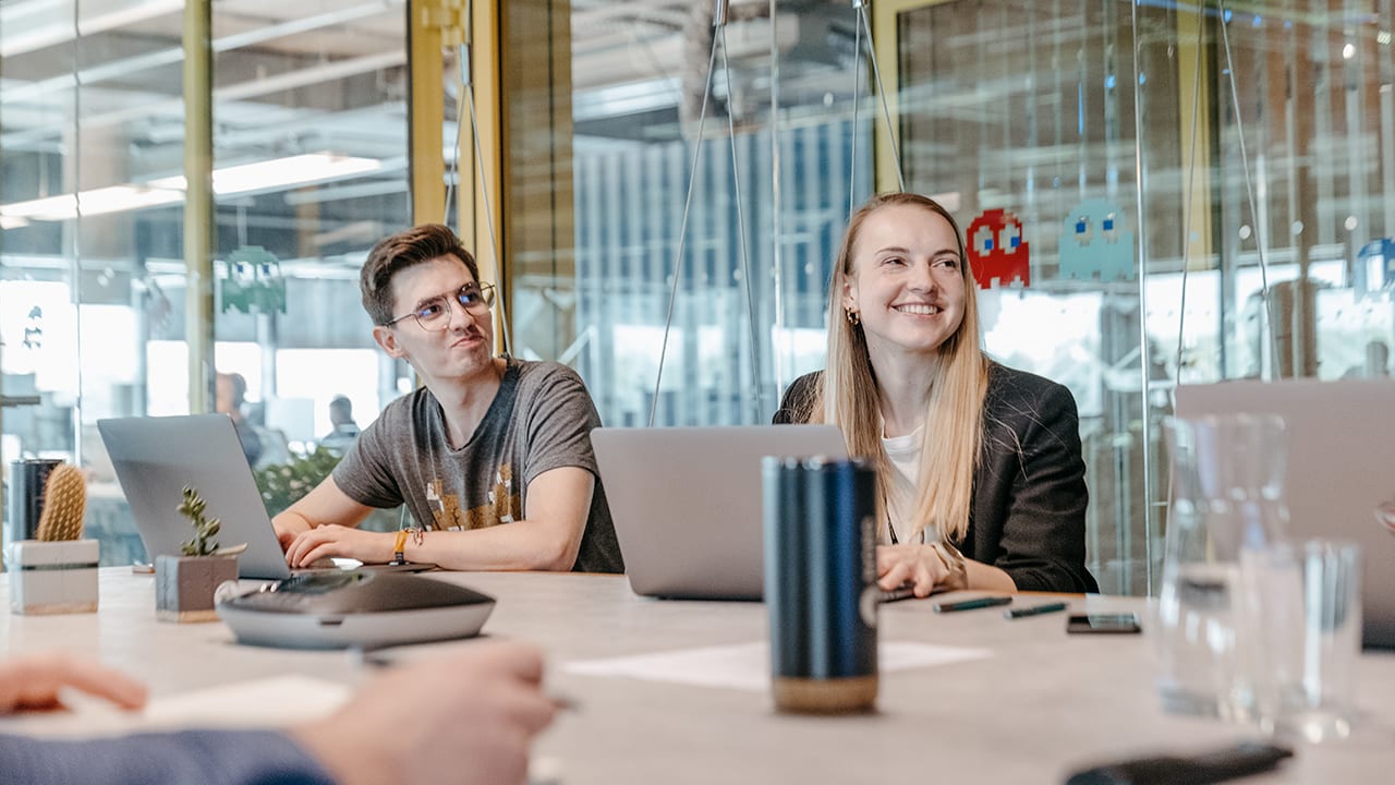 man and woman sitting in meeting room in modern glassy office smile and look off camera