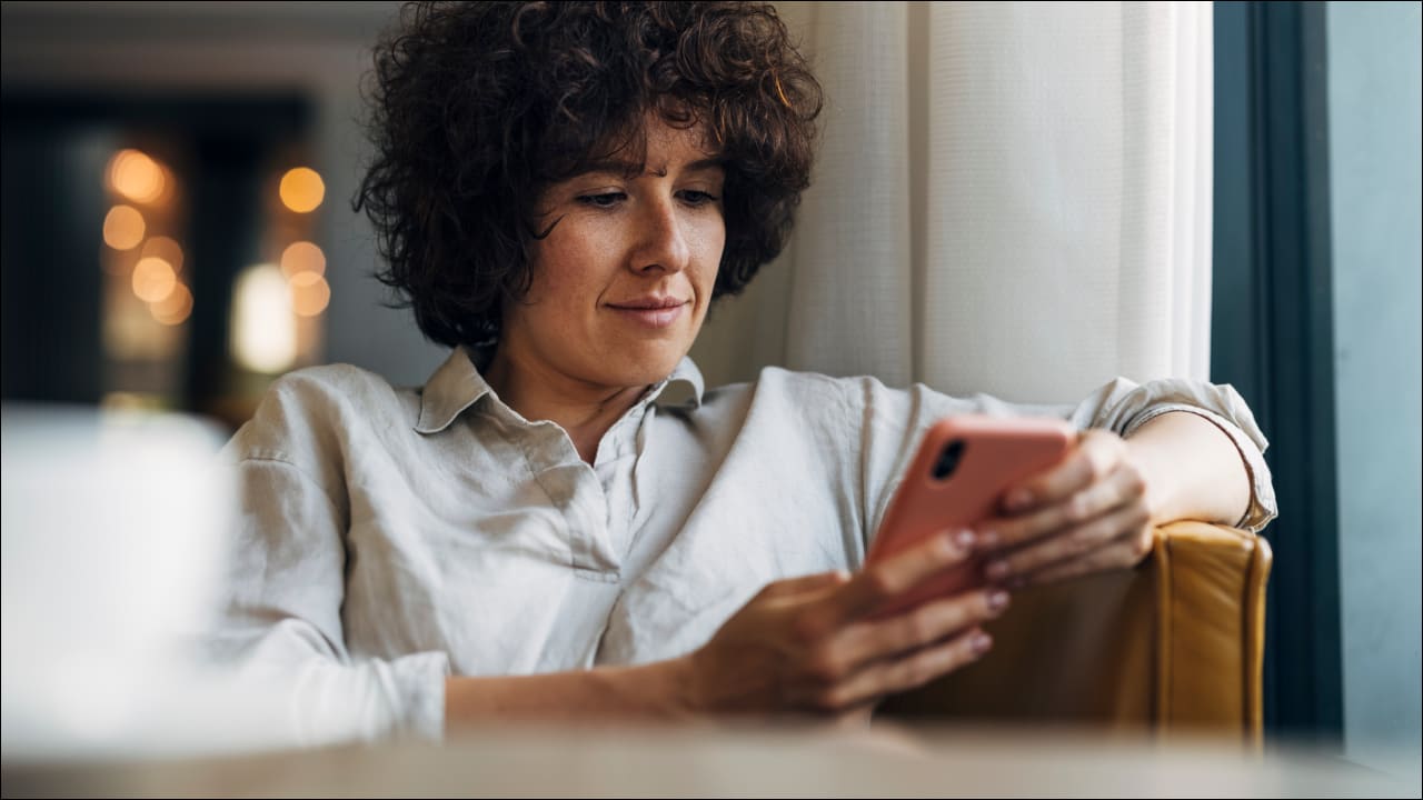 Woman sits on sofa and uses her smartphone with a smile on her face.