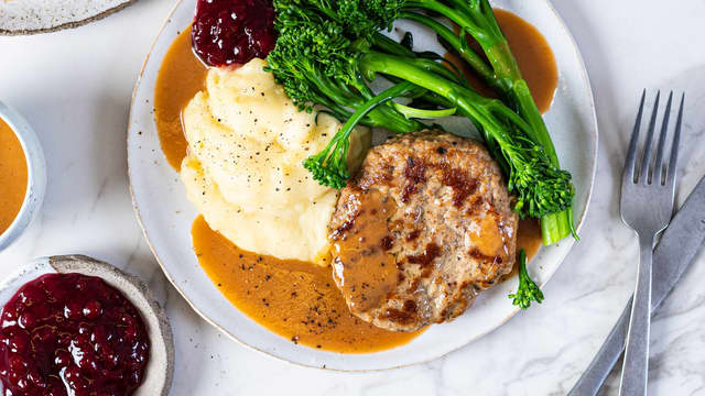 Server burgeren med brun saus, potetmos, brokkolini og tyttebærsyltetøy.