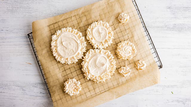 Løft den største bunnen forsiktig over på et fat. Bre over et jevnt lag med pisket krem og dryss over friske bær. Legg på neste bunn og gjenta prosessen til du har bygget et pent lite «juletre». Drypp til slutt over litt bringebærsaus og dryss over melis. Server pavlovaen med en gang.