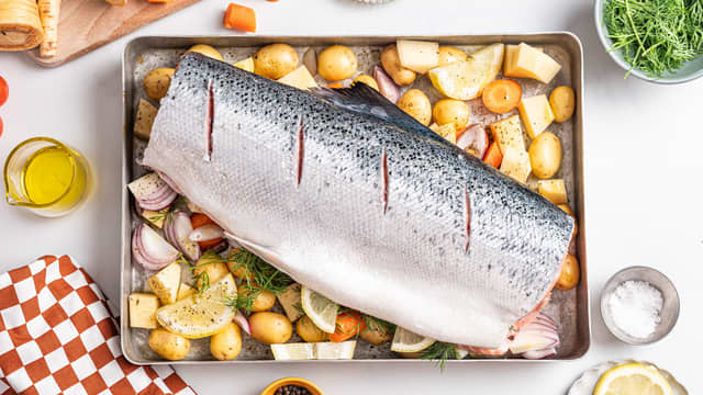 Skjær av hodet og halen på laksen med en skarp kniv. Lag snitt i skinnet på fisken, og legg den oppå grønnsakene.