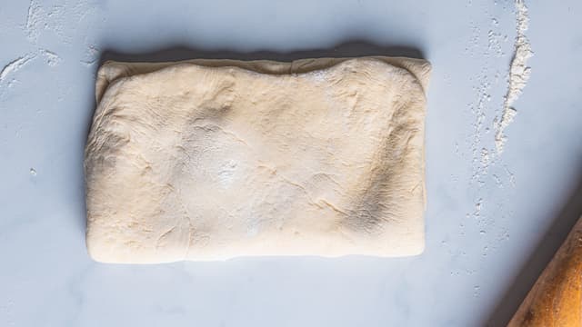 Ha mel på benken og legg deigen på bordet. Dra den ene enden av deigen ut og brett den inn mot midten. Fortsett til du har brettet den inn fire ganger.