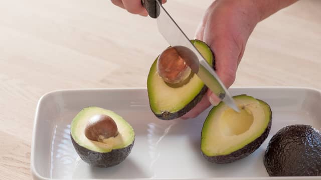 Del avokadoen i to, fjern steinen og skrap ut kjøttet med en skje. Mos avokadokjøttet i en skål eller rett på skiva med en gaffel.