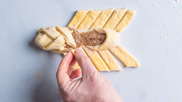 Brett endene over mandelfyllet, og begynn å brette annenhver strimmel fra toppen og ned.