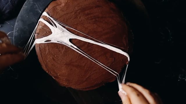 Når marshmellowstrådene er lange nok, legger du dem ned på kaken. Gjenta til du har fått kul spindelvevpynt på hele kaken.