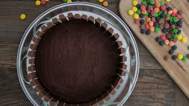 Plasser Kvikk-Lunsj pent rundt hele kanten på kaken, én og én stav med sjokolade av gangen. Dytt dem litt inn i glasuren så de sitter godt.