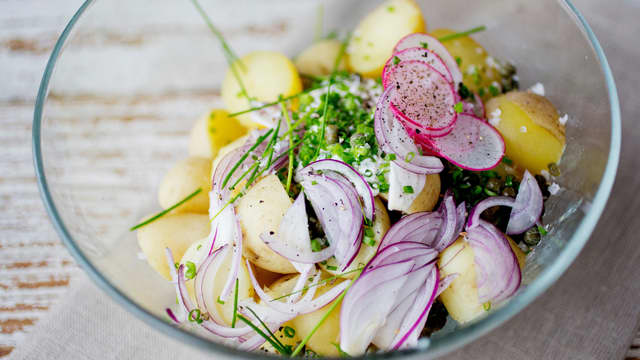 Ha potetene over i en liten bolle og tilsett creme fraiche, skivede reddiker, finsnittet rødløk, finsnittet vårløk, grovhakket gressløk, en god klype flaksalt og litt kvernet pepper.