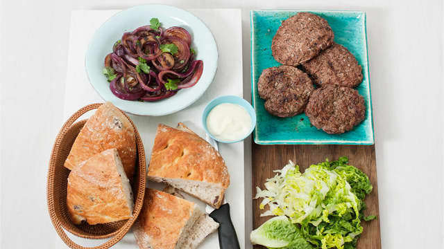 Varm focacciaen på grillen eller i ovnen på 200 grader. Del focacciaen i fire biter og snitt bitene på langs. Strimle og anrett salat på brødbunnene, topp med burgere, grillet løk, aioli og brød.