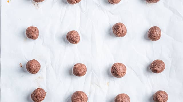 Rull små baller som legges på et bakebrett med bakepapir.