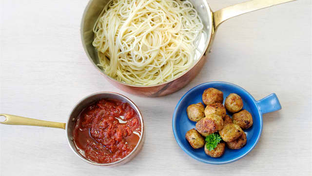 Kok spagetti etter anvisning på pakken, varm pastasausen i en kjele og anrett på tallerkener med noen kjøttboller på toppen.