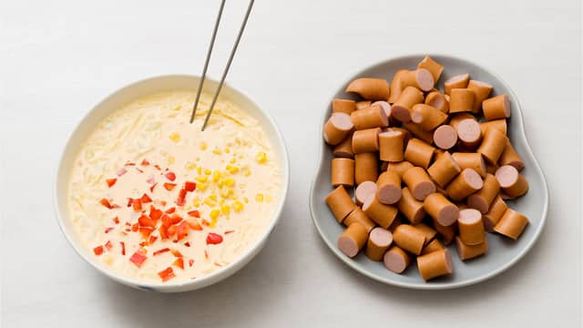 Visp sammen fløte, egg og pesto, vend inn pølsebitene, godt avrent mais, grønnsaker og ost.