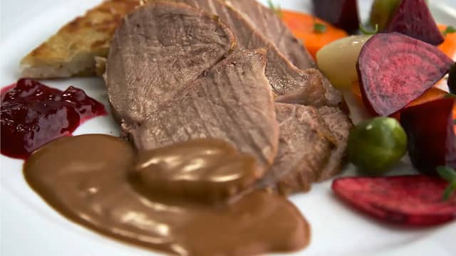 Skjær steken i skiver og server med saus, røstipoteter, glaserte beter og grønnsaker.