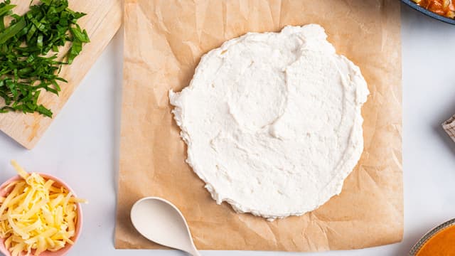 Trykk ut litt av deigen på et bakepapir og fordel den utover til en sirkel. Bruk baksiden på en skje eller en slikkepott.