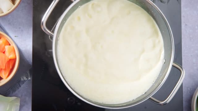 Kok opp fløte og fiskebuljong i en kjele.