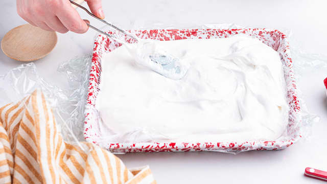 Ha marshmallowsmassen i formen, og smør den utover med en slikkepott. Dryss melis på toppen.