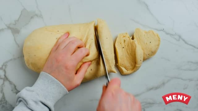 Kna deigen raskt sammen, og form til en avlang deig. Del så i biter og form 15-20 boller.