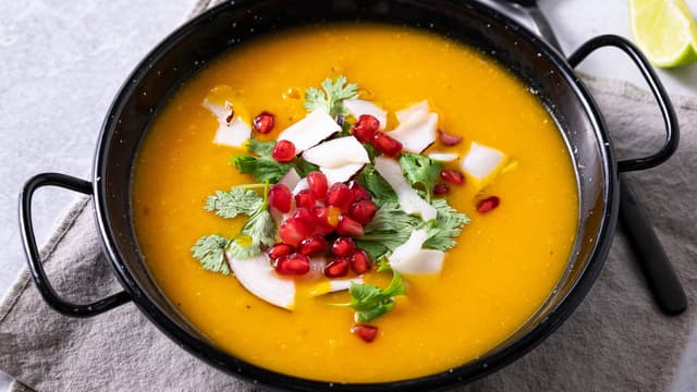**Topp suppen** med et dryss av hakket koriander, kokosflak og granateplekjerner.