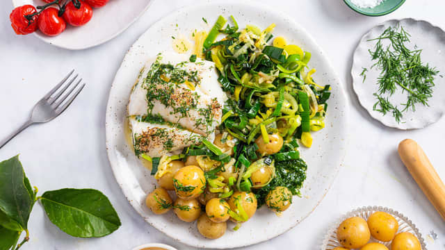 Server skreiloinen med stekt purre, kokte poteter, bakte tomater og urtesmør.