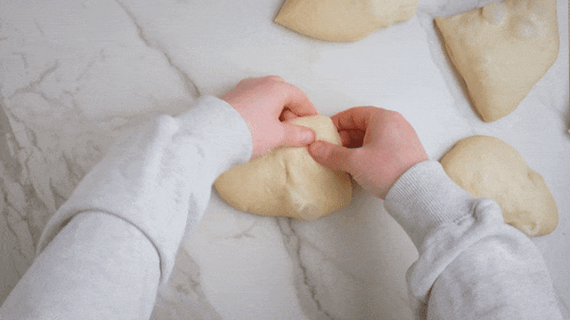 Bruk en slikkepott eller litt mel på fingrene og brett alle fire sidene av deigen inn mot midten. Snu emnene slik at de ligger med bretten ned på bakepapiret.