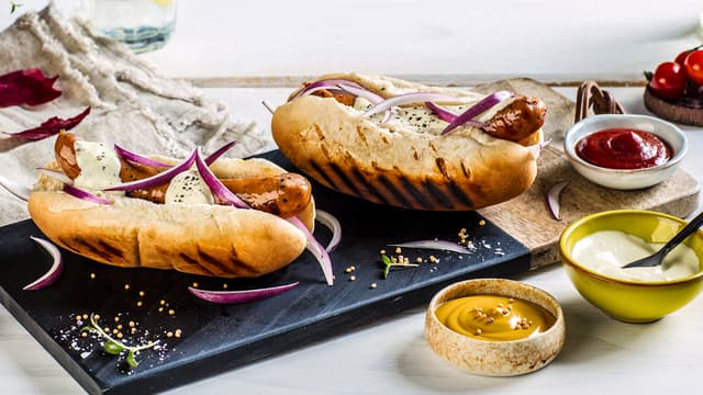 Varm pølsebrødene raskt på grillen og del rødløken i båter.