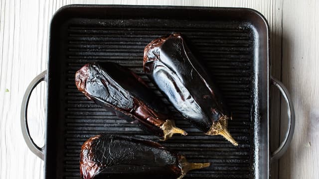 Legg hele auberginer på grillen eller i en varm jernpanne. Grill auberginene over middels høy varme til de blir helt myke over det hele, det tar ca. 1 time. Snu auberginene etter hvert som du ser de faller sammen. Er du usikker på om de er ferdige, kan du la dem ligge litt til.