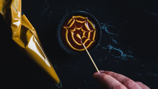 Ha ketchup i en skål, og lag spindelvevmønster med sennep.