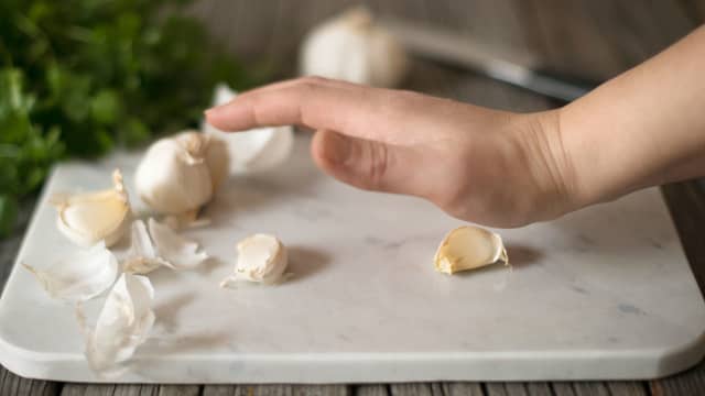 Knus de uskrelte hvitløkfeddene med bredsiden av en kniv, og del løken i to.