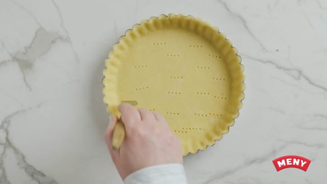 Prikk bunnen med en gaffel, kle den med bakepapir og dekk bunnen med tørkede erter (for at bunnen skal bevare fasongen under steking).