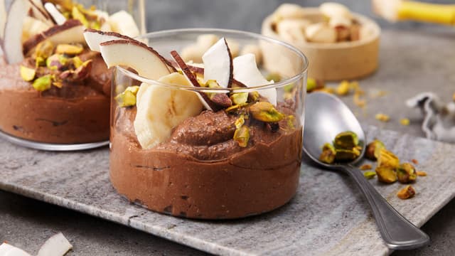 Fordel sjokolademoussen i to glass eller skåler, og topp med litt skivet banan, kokosflak og hakkede nøtter.