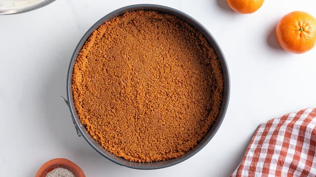 Dekk bunnen av en kakeform med bakepapir. Ha pepperkakesmulene i formen og press jevnt utover bunnen med en slikkepott. Press gjerne litt av bunnen oppover kantene også.