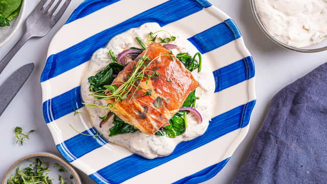 Anrett rekesausen på to tallerkener og topp med spinat, løk og stekt torskefilet. Pynt med friske urter og gjerne litt ekstra reker.