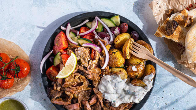 Anrett shawarma, stekte poteter, bakte tomater, gresk salat og tzatziki på to tallerkener.