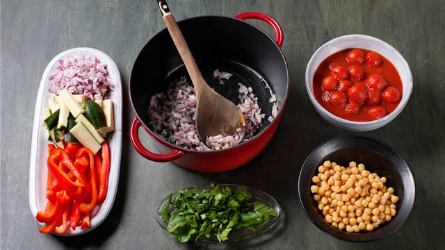 **Kutt opp og stek grønnsakene:** Hakk persille, finhakk rødløk, skjær paprika og squash i strimler og fres i olje i ca. 2-3 min. Vend inn persille, kokte kikerter og hermetiske tomater.