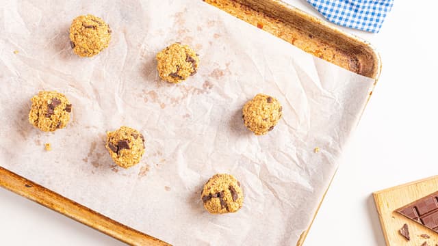Rull sammen boller av deigen med hendene og legg bollene på et bakebrett med bakepapir. Klem bollene flate.