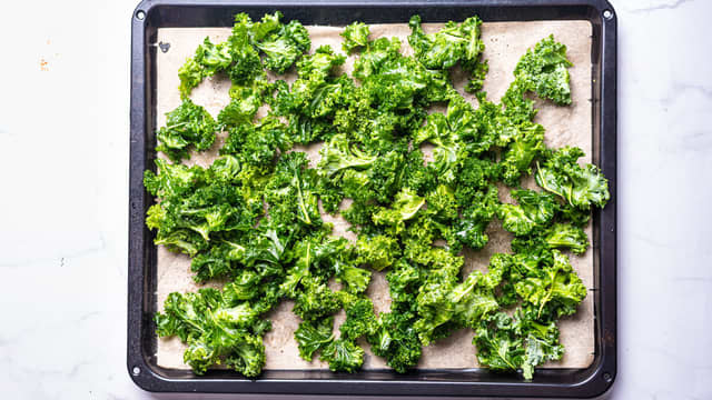 Dra bladene av grønnkålkvastene, prøv å få med så lite harde stilker som mulig. Fordel halvparten av grønnkålbladene på stekebrettet.