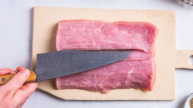 Skjær et snitt på langs av svinefileten. Skjær fileten slik at den blir et avlangt kjøttstykke som er like tykt over hele.