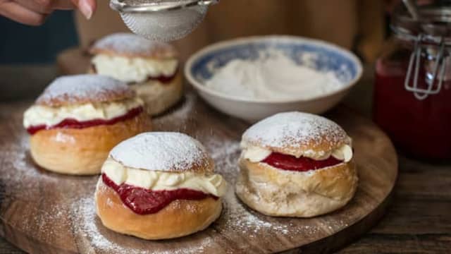 Del bollene i to, smør på bringebær- eller jordbærsyltetøy på bunnen, og topp med et par spiseskjeer med vaniljekrem. Legg på toppen av bollen og strø melis over.