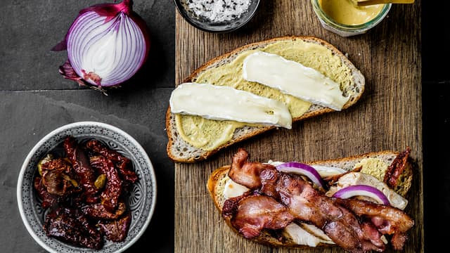 Legg skivet rødløk, soltørket tomat, kylling og sprøstekt bacon på, og topp med to osteskiver og en skive brød som har sennepsiden ned. Krydre med salt og pepper.