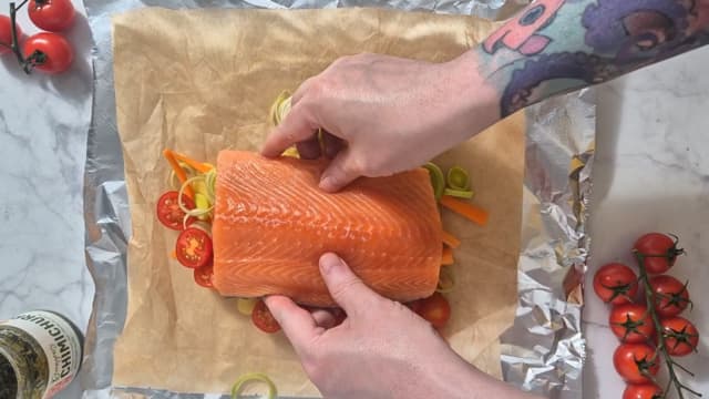 Legg laksefileten oppå grønnsakene. Fordel chimichurri over laksen. Brett bakepapiret og folien tett sammen til en pakke.