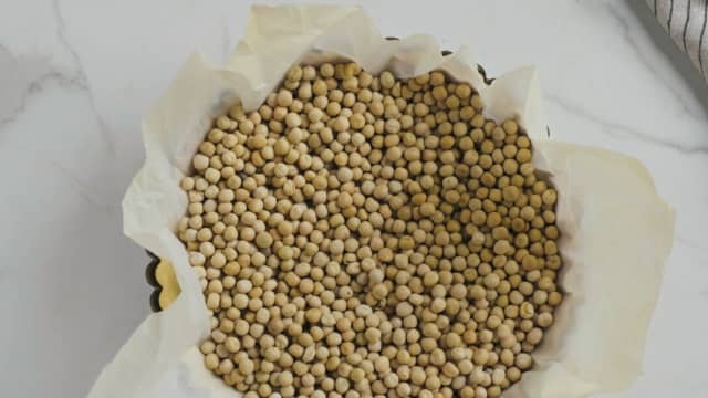 Prikk bunnen med en gaffel. Kle den så med bakepapir og dekk bunnen med tørkede erter.