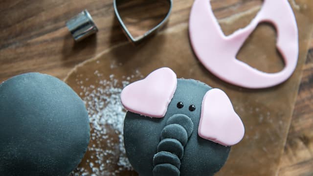 Hull ut flere små sirkler til snablen og hull ut hjerter av rosa fondant til elefantører. Øyne tegnes på med farget glasur.