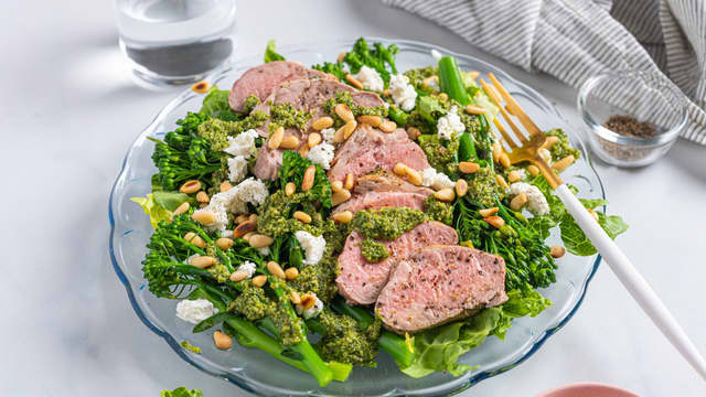 Topp salaten med skiver av svinefilet, chevre, pesto og ristede pinjekjerner.