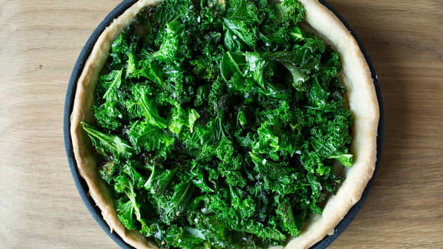 **Fyll:** Fres grønnkål til den blir blank i en stor stekepanne med litt olivenolje. Tilsett hvitløk og rør til grønnkålen mykner noe. Fordel grønnkålen utover tertebunnen og dryss over osten.