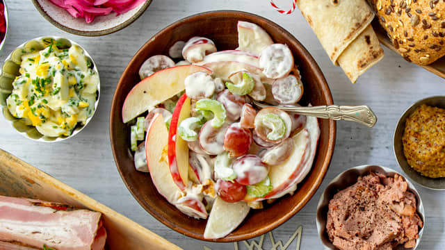 Skjær eplene i tynne skiver og del druene i to. Fjern de groveste trevlene på stangsellerien og skjær den i tynne skiver. Pisk fløten til en myk krem og vend majonesen inn i kremen. Smak til med noen dråper sitronsaft og en god klype sukker. Bland alle ingrediensene lett sammen, vend inn grovhakkede valnøtter.